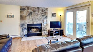 Ein Wohnzimmer mit Kamin aus Stein, einem Fernseher, Ledersofas und einer Schiebetür zu einem Außenbereich.