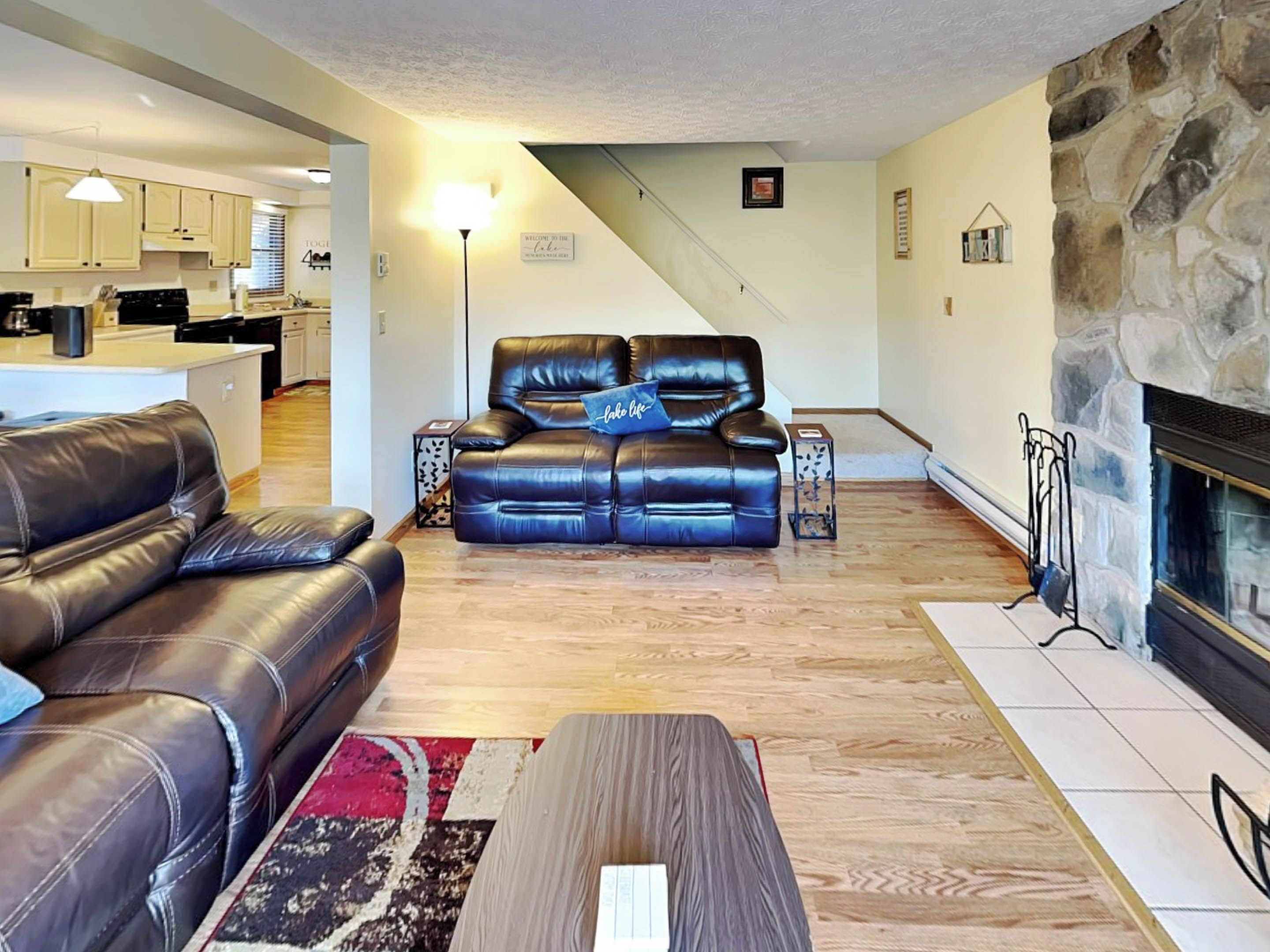 A living room with a black leather sofa, a wooden coffee table, and a stone fireplace.