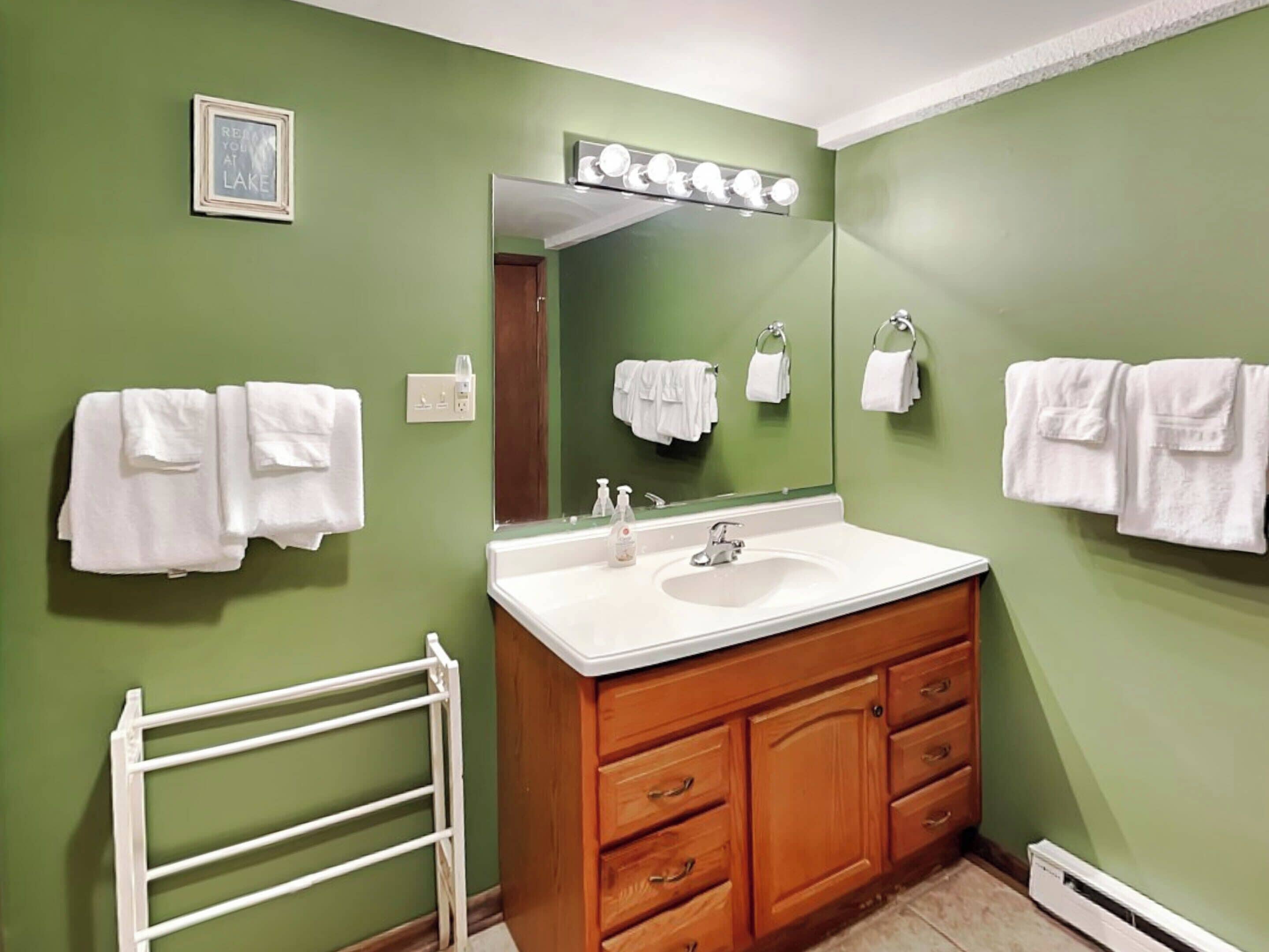 A bathroom with a green wall, a white sink, wooden cabinets, and a white towel rack.