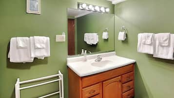 A bathroom with a green wall, a white sink, wooden cabinets, and a white towel rack.