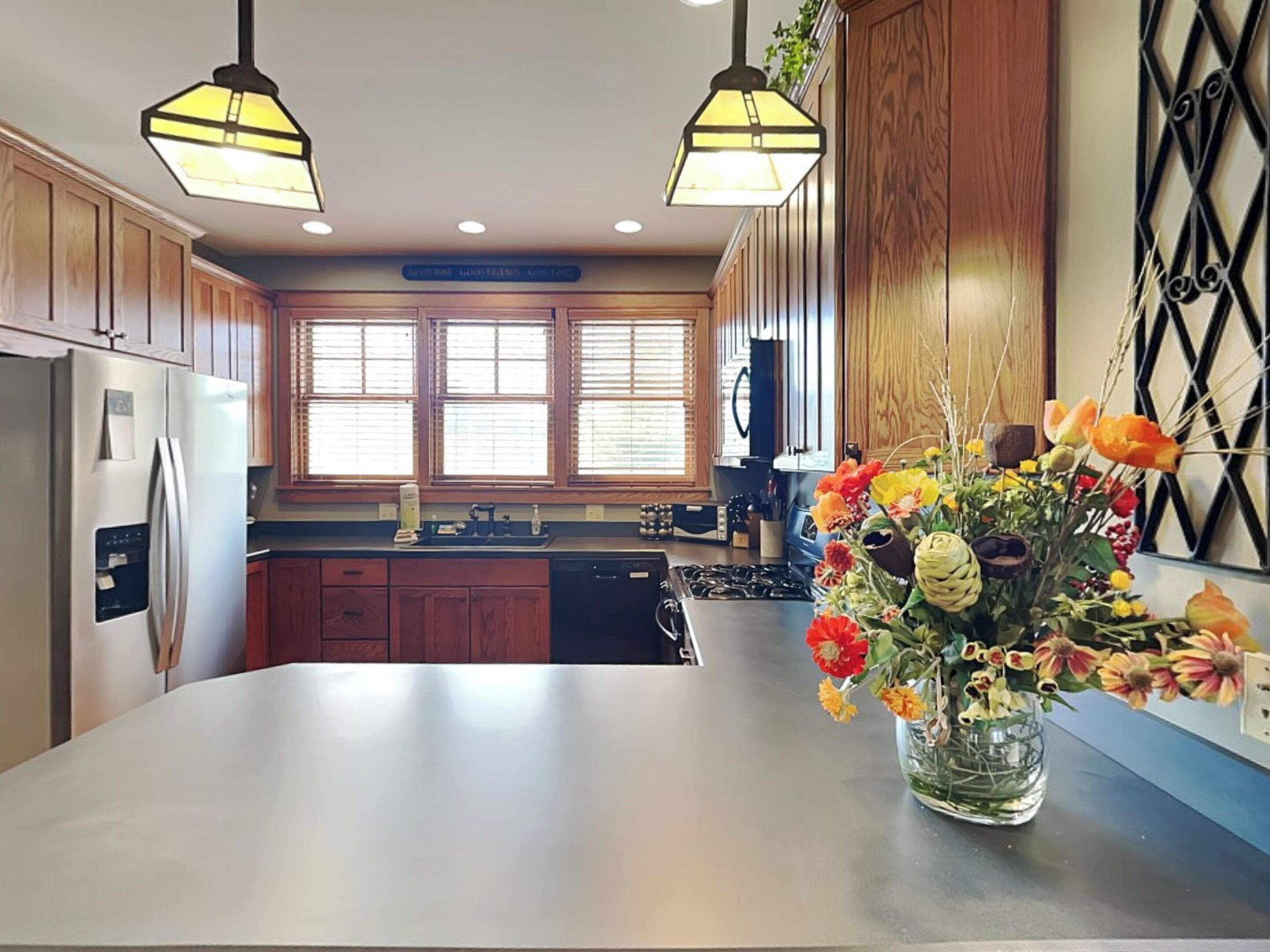 Una cocina con gabinetes de madera, un refrigerador de acero inoxidable, una estufa y un florero con flores en la encimera.