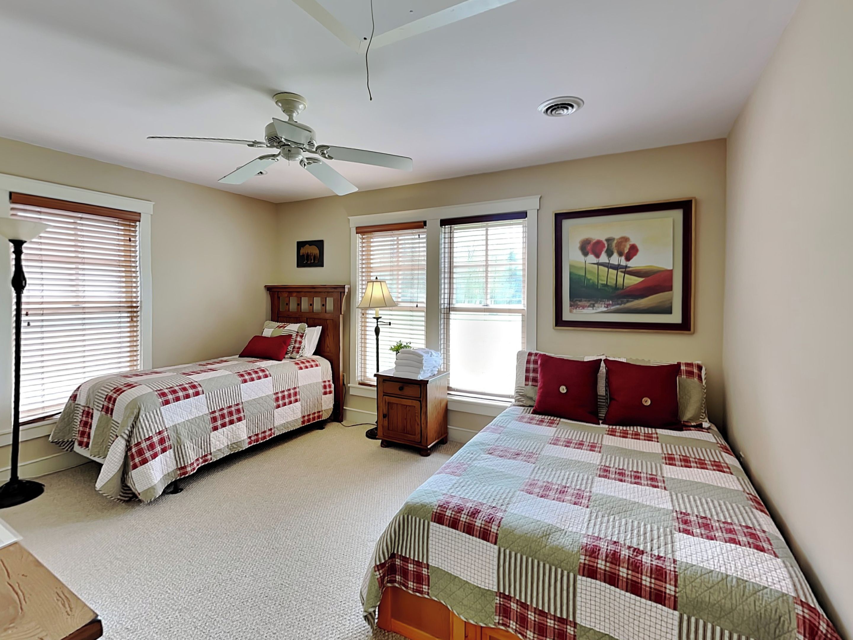 A bedroom with two beds, a ceiling fan, a nightstand, a lamp, and a painting on the wall.