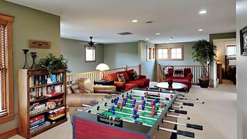 A cozy living room with a foosball table, a bookshelf, a red sofa, and a coffee table.