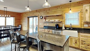 A modern kitchen with wooden paneling, a central island with bar stools, pendant lighting, and built-in appliances. - Space Mountain by Taylor Made Deep Creek (McHenry)