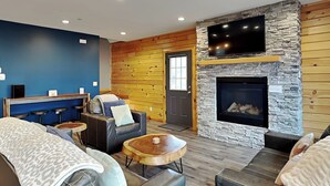 A modern lounge area with a stone fireplace, leather seating, and a flat-screen TV mounted on a stone wall. - Space Mountain by Taylor Made Deep Creek (McHenry)