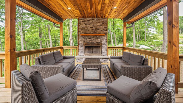 A covered outdoor seating area with wicker furniture and a stone fireplace. - Space Mountain by Taylor Made Deep Creek (McHenry)