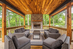 A covered outdoor seating area with wicker furniture and a stone fireplace. - Space Mountain by Taylor Made Deep Creek (McHenry)