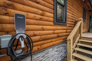 A JuiceBox charging station attached to a wooden cabin wall with a stone foundation. - Space Mountain by Taylor Made Deep Creek (McHenry)