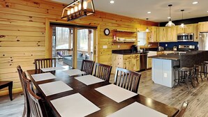 A modern log cabin with a dining area, kitchen, and a large window overlooking a deck. - Space Mountain by Taylor Made Deep Creek (McHenry)