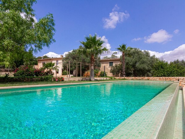 A clear blue swimming pool with a tiled edge, surrounded by lush greenery and a stone wall. - Villa Son Brun near the Rafa Nadal Academy (Manacor)