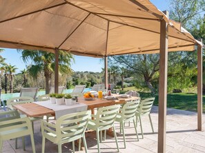 An outdoor dining area with a table and chairs under a large canopy, overlooking a pool and lush greenery. - Villa Son Brun near the Rafa Nadal Academy (Manacor)