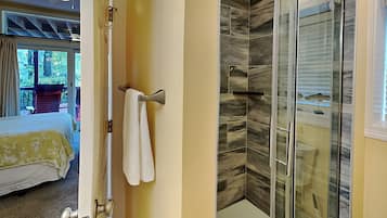A hotel room with a bed, a bathroom with a glass shower enclosure, and a view of the outdoors.