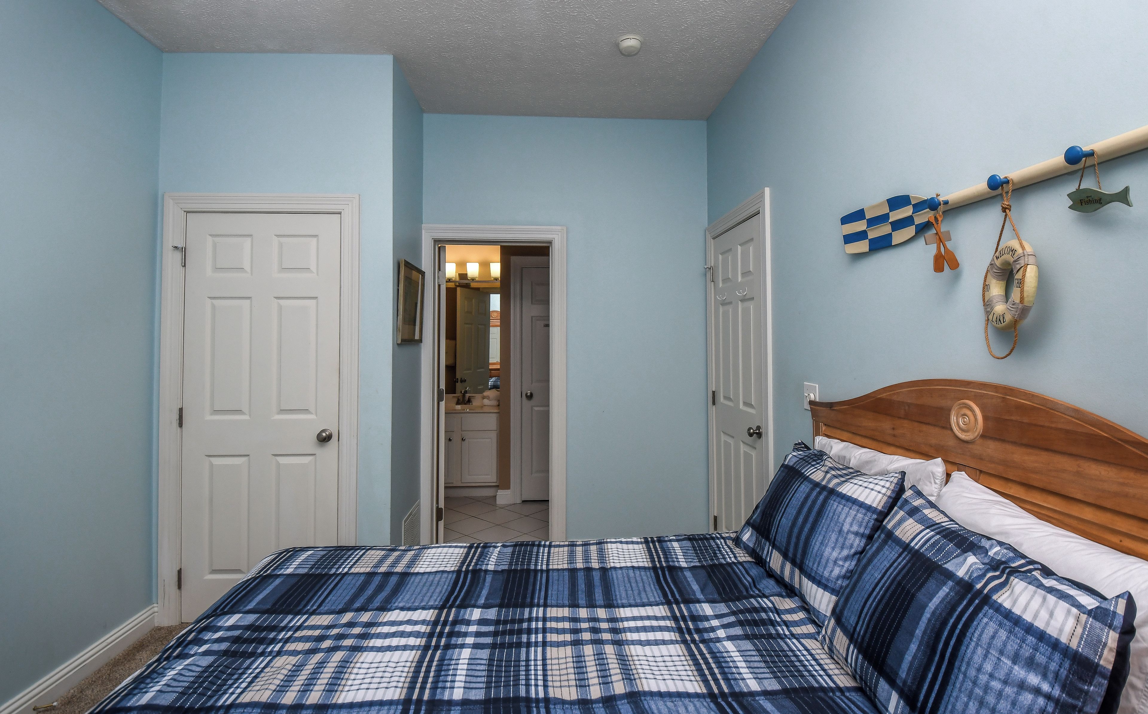 A bedroom with a bed, two doors, a hallway, and a wall with a fish-shaped decoration.