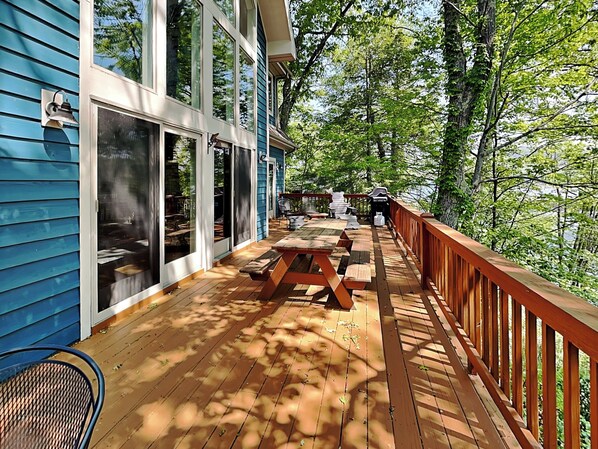 A wooden deck with picnic tables and a railing, overlooking a forested area.
