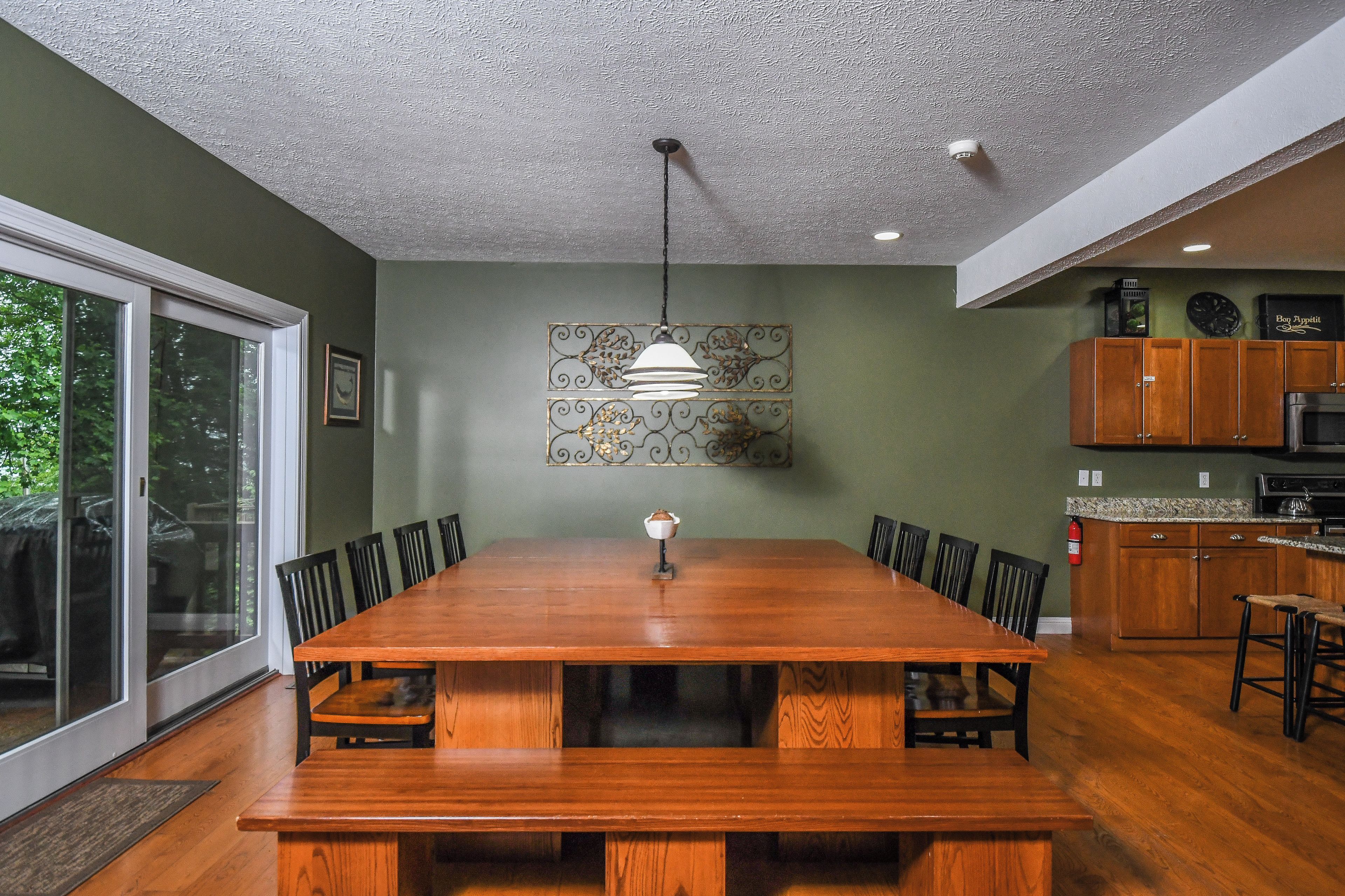 A dining area with a wooden table and chairs, a pendant light, and a view of the outdoors through a sliding glass door.