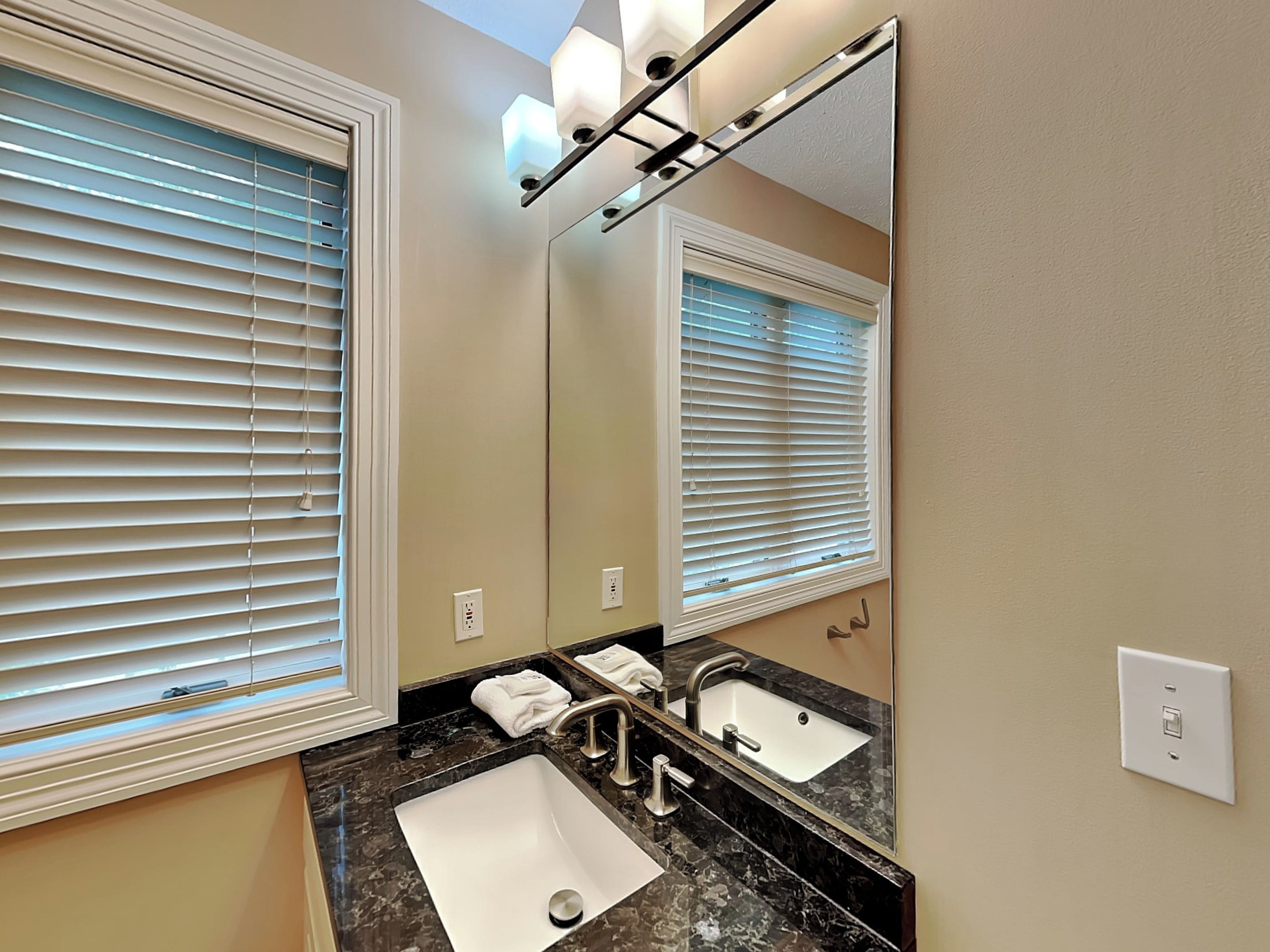 A bathroom with two sinks, a large mirror, and blinds on the windows.