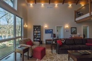 A spacious living room with a large window, a bookshelf, a sofa, and a coffee table. - Stargazer by Taylor Made Deep Creek (Oakland)