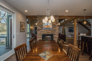 A spacious dining area with a long wooden table, stone fireplace, and a view of the outdoors.