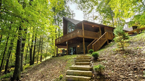A cabin with a wooden exterior, a balcony, and a stone staircase leading up to it. - Stay Awhile by Taylor Made Deep Creek (McHenry)