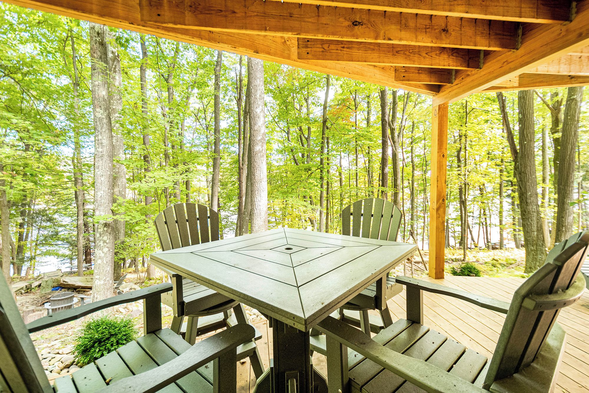 A wooden deck with a picnic table and chairs, surrounded by trees.