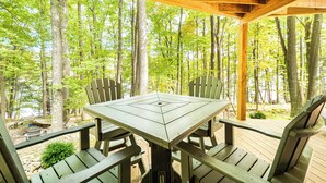 A wooden deck with a picnic table and chairs, surrounded by trees. - Stay Awhile by Taylor Made Deep Creek (McHenry)