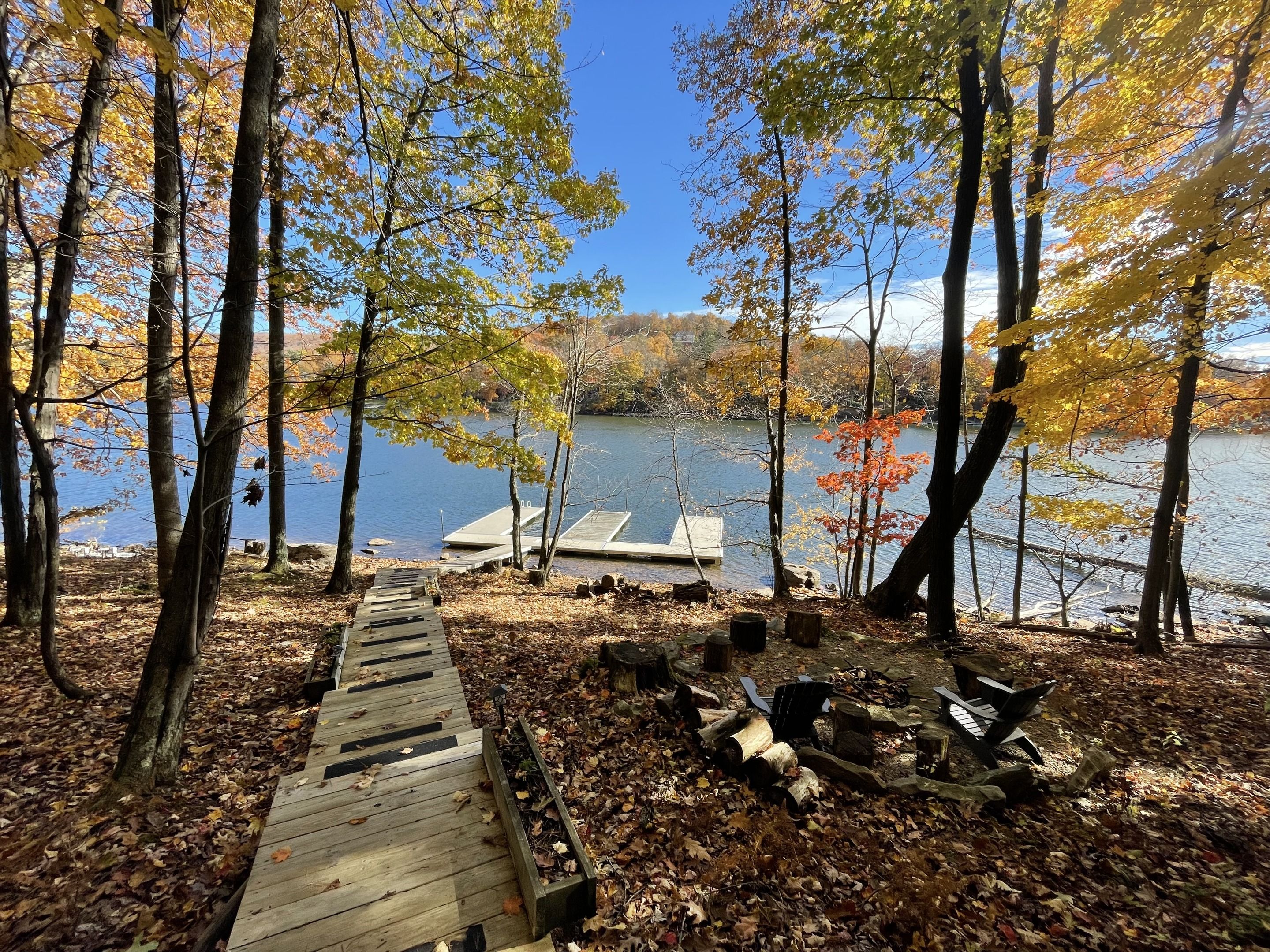 A wooden dock leading to a docked boat on a calm lake surrounded by trees with autumn leaves.