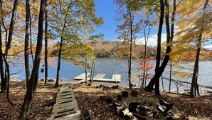 A wooden dock leading to a docked boat on a calm lake surrounded by trees with autumn leaves. - Stay Awhile by Taylor Made Deep Creek (McHenry)
