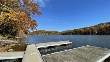 A wooden dock extending into a calm lake, surrounded by autumn-colored trees and hills in the background.