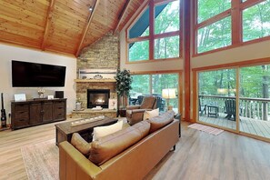 Un salón comedor amplio con chimenea de piedra, sofá de cuero y ventanas grandes con vistas a una terraza.