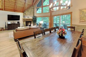 Un salón espacioso con una gran mesa de comedor de madera, chimenea y televisor montado en la pared.