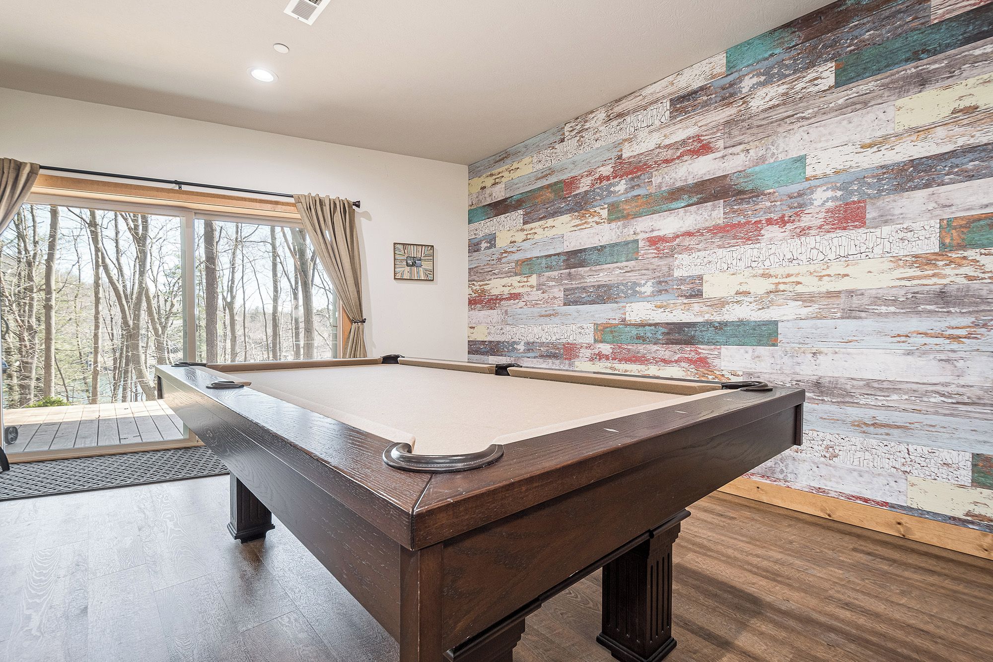 A pool table in a room with a large window, a rustic wall, and a small clock.