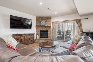 Una sala de estar con chimenea de piedra, un televisor de pantalla plana, sofás de cuero y vistas al exterior.