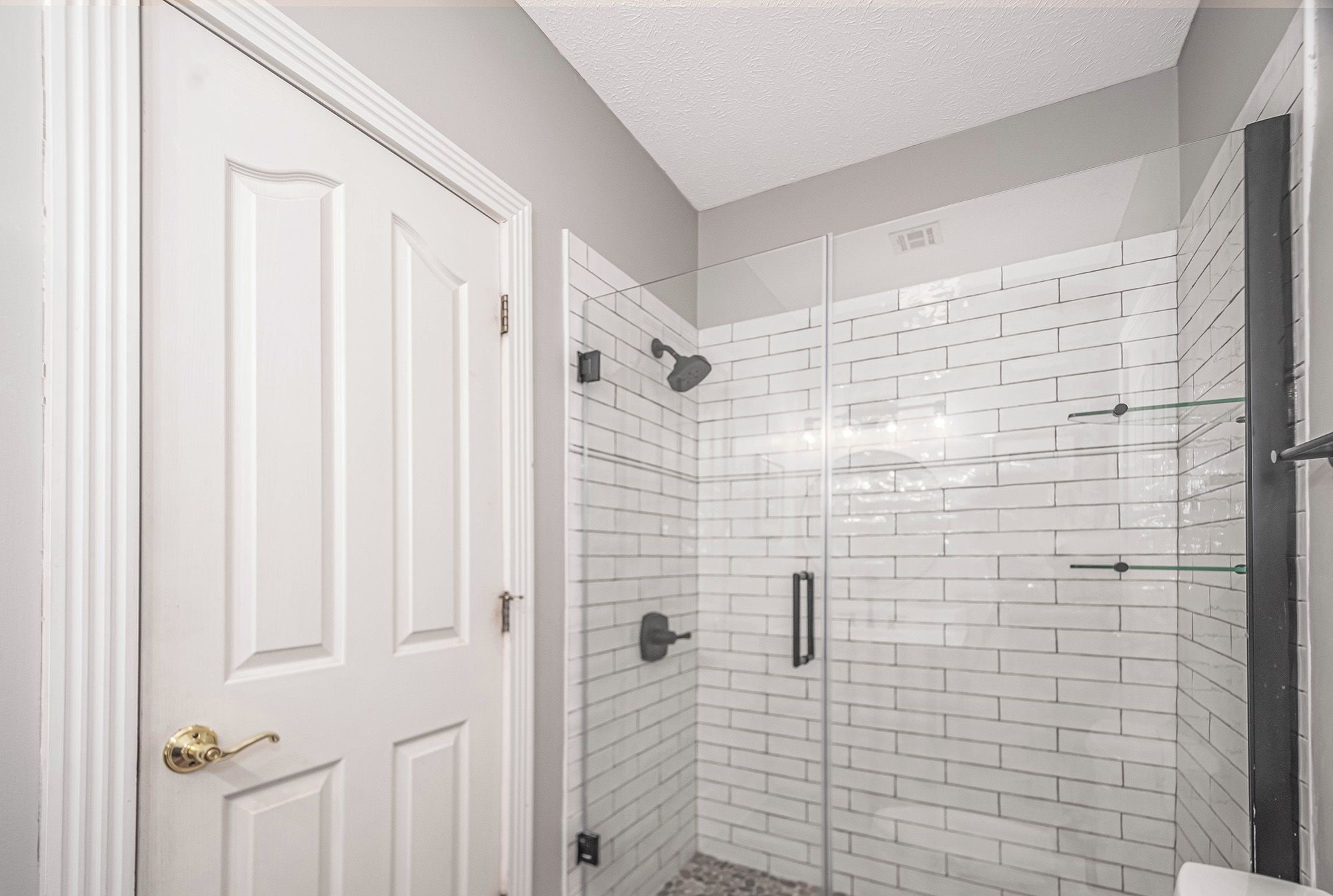 A bathroom with white subway tile walls, a glass shower enclosure, and a white door with a brass handle.