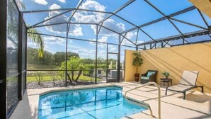 A covered outdoor pool area with a glass enclosure, lounge chairs, and a view of the surrounding landscape.