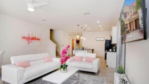 A modern living room with white sofas, a coffee table, and a staircase leading to a kitchen.