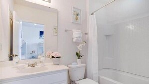 A bathroom with a white sink, toilet, and bathtub. There are decorative flowers on the sink and a towel rack on the wall.