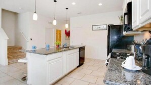 A modern kitchen with white cabinets, a granite countertop, and a central island. There are pendant lights, a microwave, and a coffee maker on the countertop.