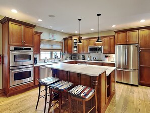 A modern kitchen with wooden cabinets, stainless steel appliances, and a central island with bar stools. - Stone Mountain Vista by Taylor Made Deep Creek (McHenry)