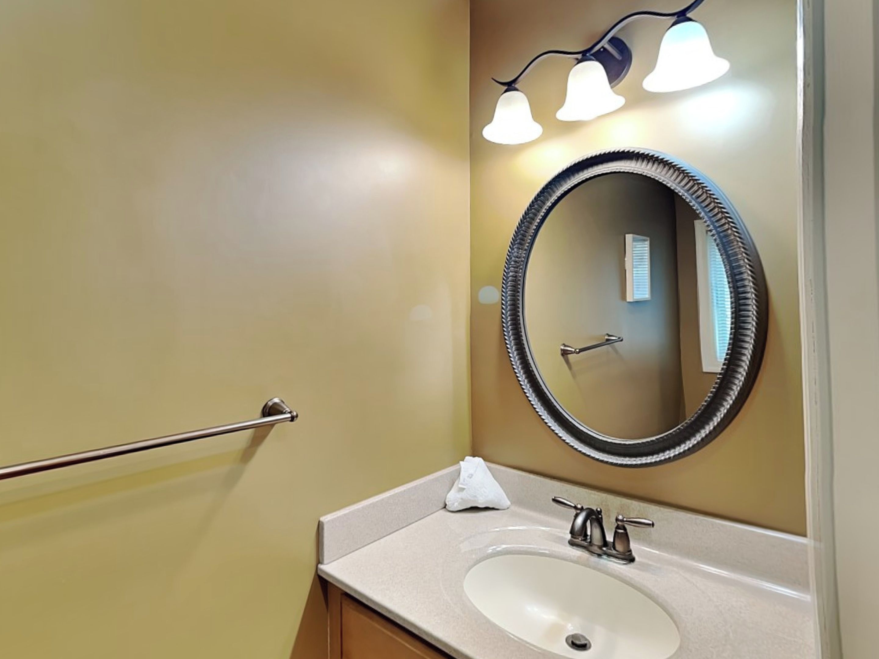 A bathroom with a round mirror, a sink, and a towel rack.