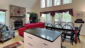 Uma sala de estar ampla com lareira de pedra, um sofá vermelho, uma mesa de jantar com cadeiras e uma ilha de cozinha.