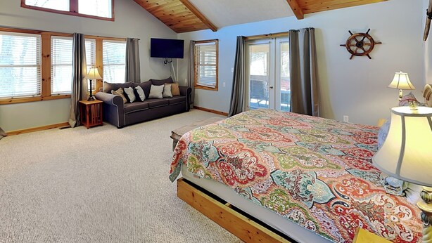 A bedroom with a bed, a sofa, a TV, a ceiling fan, and large windows. - Sunkissed Lodge by Taylor Made Deep Creek (McHenry)