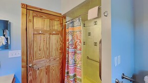 A bathroom with a wooden door, a shower with a colorful shower curtain, and a toilet with a towel rack. - Sunkissed Lodge by Taylor Made Deep Creek (McHenry)