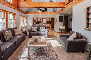 A spacious living room with a large sofa set, a coffee table, and a view into the kitchen.