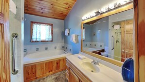 A bathroom with a bathtub, a sink, wooden cabinets, a mirror, and a window with curtains. - Sunkissed Lodge by Taylor Made Deep Creek (McHenry)