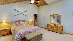 A bedroom with a wooden ceiling, a bed with patterned bedding, a dresser with a mirror, and a ceiling fan. - Sunkissed Lodge by Taylor Made Deep Creek (McHenry)