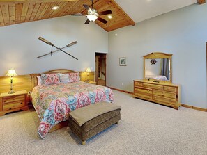 A bedroom with a wooden ceiling, a bed with patterned bedding, a dresser with a mirror, and a ceiling fan. - Sunkissed Lodge by Taylor Made Deep Creek (McHenry)