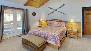 A bedroom with a bed, bedside tables, a wooden ceiling, a wall-mounted ship's wheel, and a sliding glass door. - Sunkissed Lodge by Taylor Made Deep Creek (McHenry)