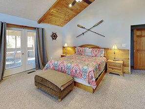 A bedroom with a bed, bedside tables, a wooden ceiling, a wall-mounted ship's wheel, and a sliding glass door. - Sunkissed Lodge by Taylor Made Deep Creek (McHenry)