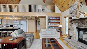 A spacious loft with a high ceiling, a kitchen area, a living room with a fireplace, and a large bookshelf. - Sunny Boy by Taylor Made Deep Creek (McHenry)