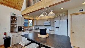 A modern kitchen with a central island, bar stools, wooden beams, and a 'Go Jump Lake' sign. - Sunny Boy by Taylor Made Deep Creek (McHenry)